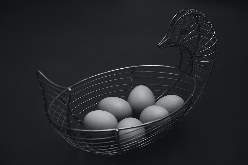 A metal basket made of wire in the shape of a hen with half a dozen eggs.