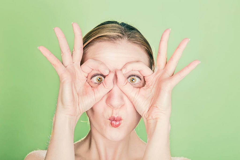 A woman holding her fingers round her eyes to imitate glasses on her face