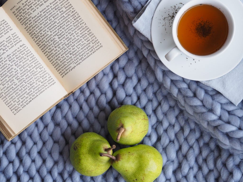 A table with pears, tea, and a book on it.