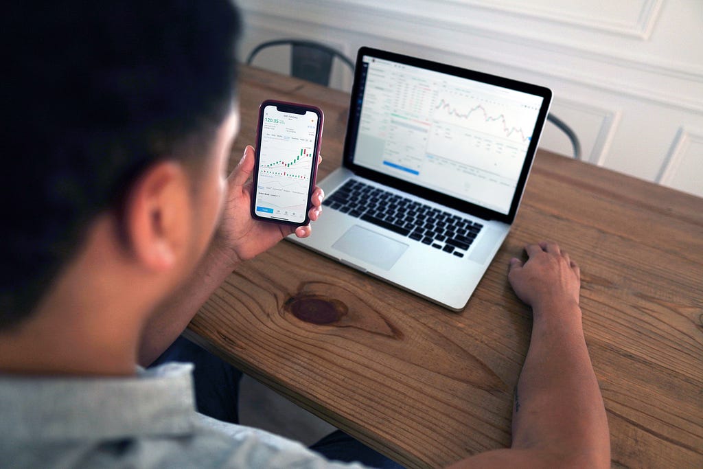 A person looking at graphs on a smartphone and a laptop