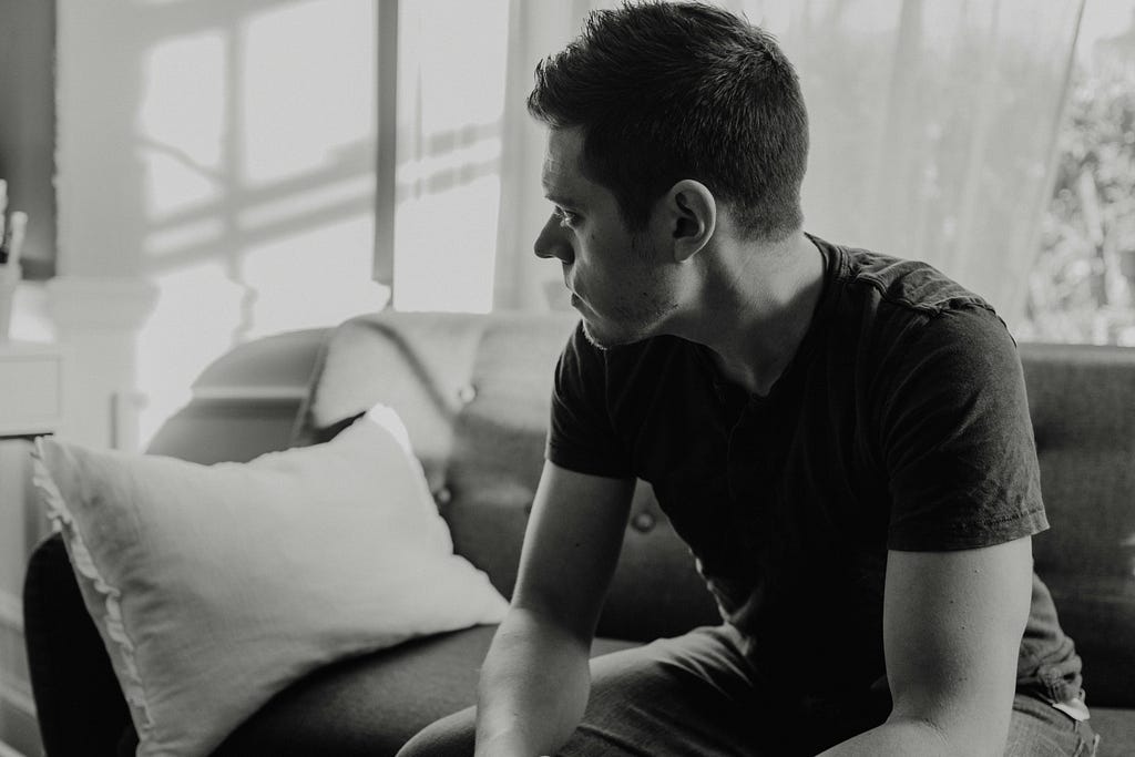 Black and white photo of man sitting on the couch, thinking