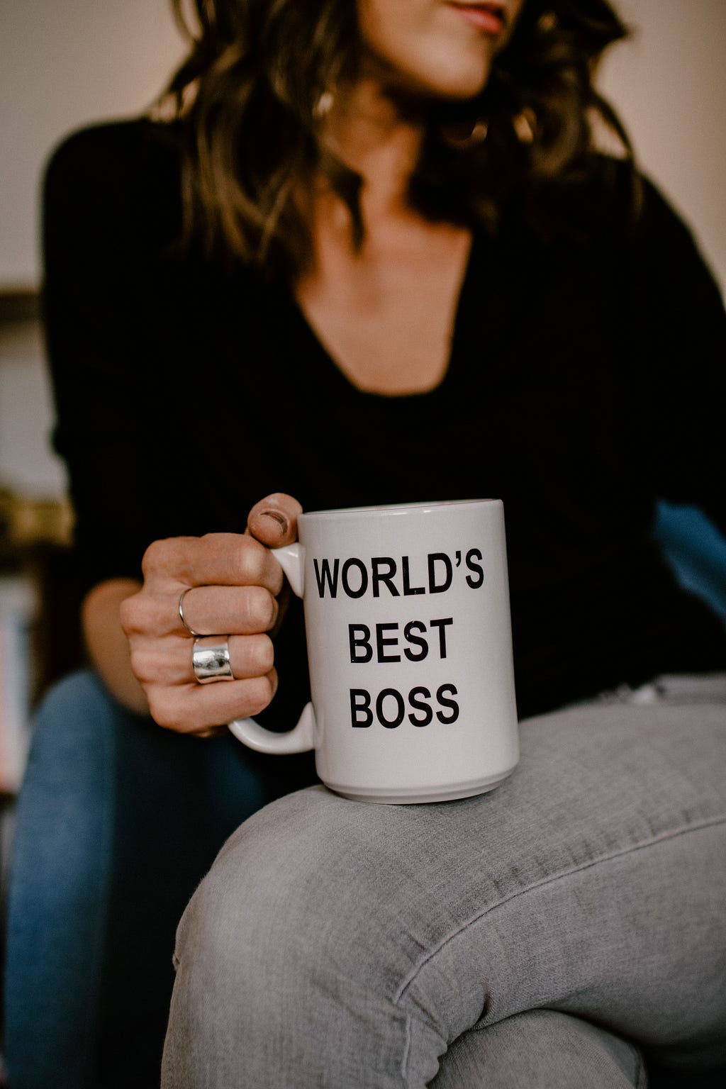 A sitting woman holds a “World’s Best Boss” mug