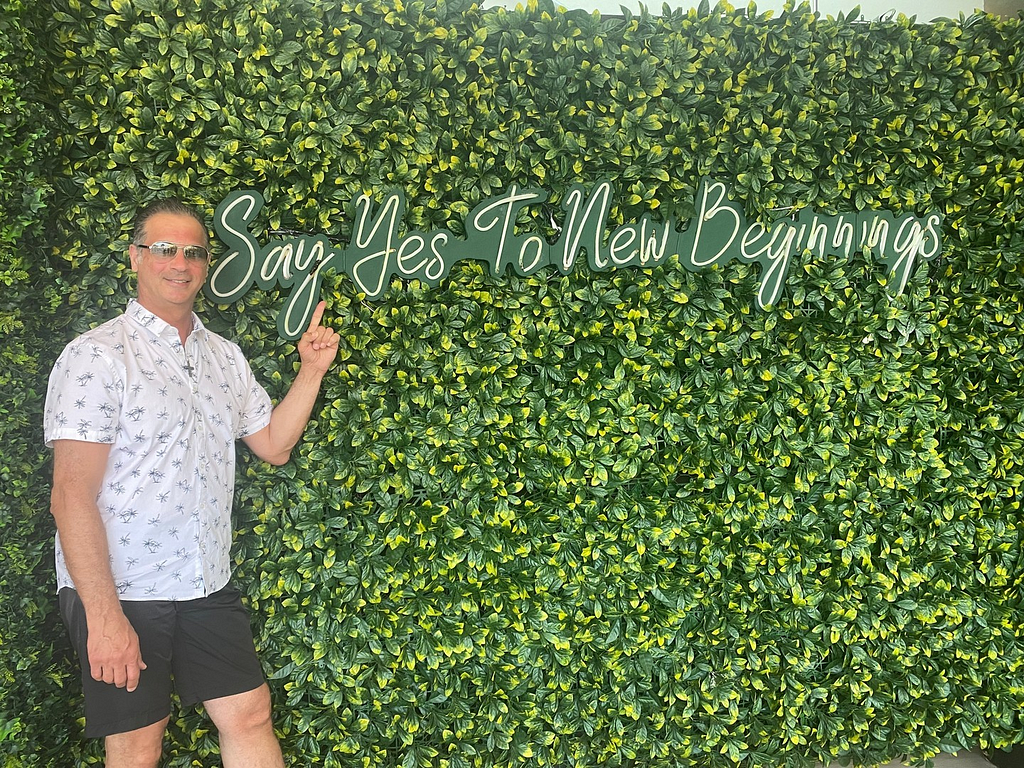 Mario Piccone pointing to a sign that says “Say yes to new beginnings”