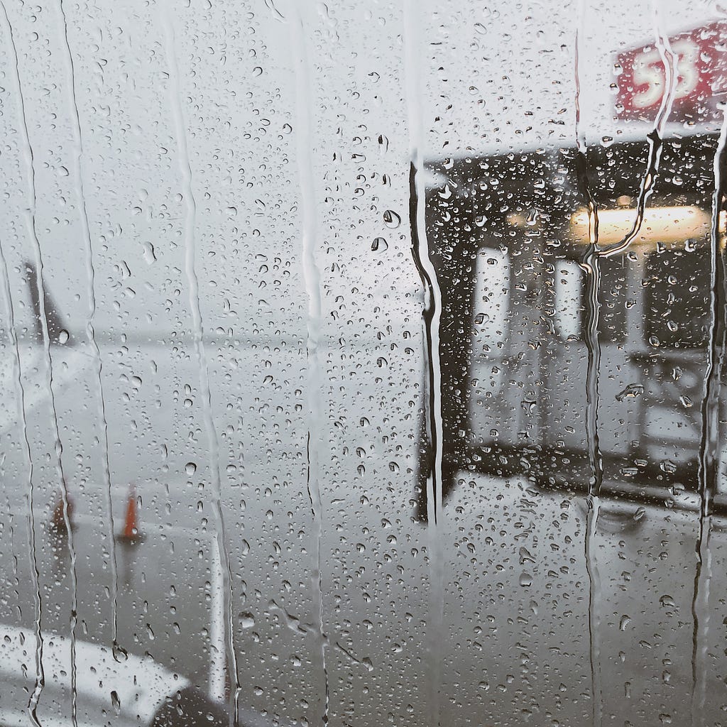 an oncoming jet bridge from the view of a rainy airplane window