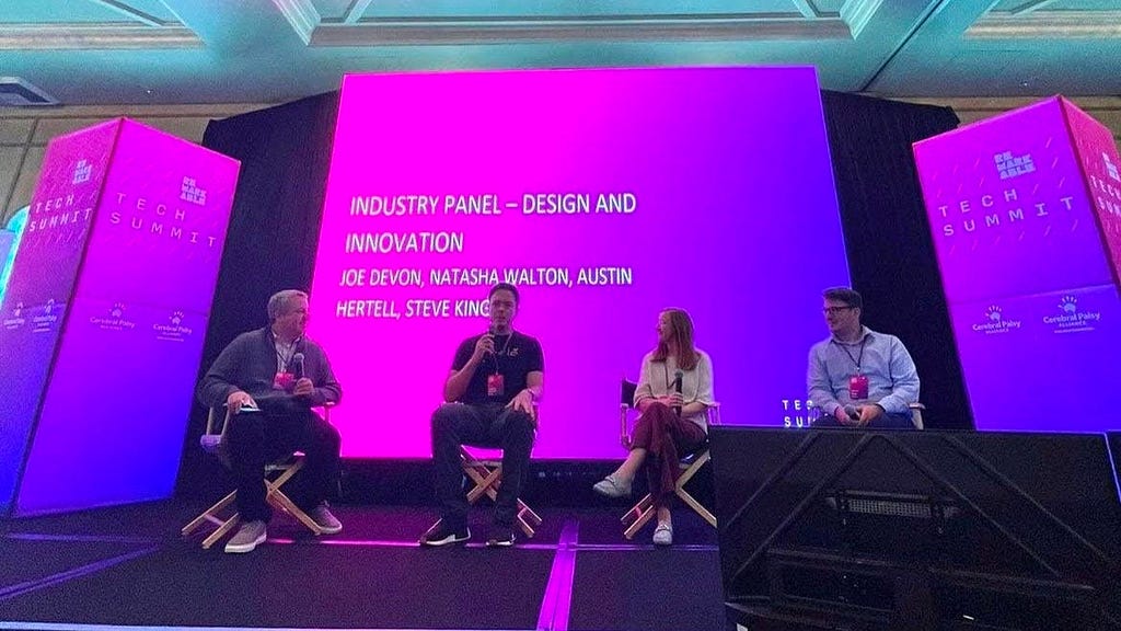 The four panel participants on stage in front of a pink and purple screen that reads “Industry Panel — Design and Innovation”