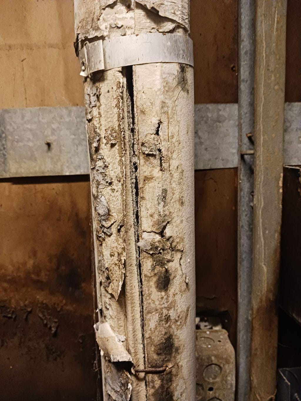 An old pipe riddled with holes, discoloration, and seeming to be barely held together.