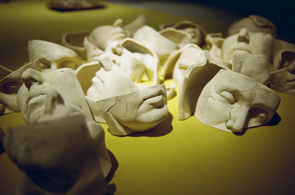 An image shows many plaster-of-paris masks  broken in half on a yellow table.