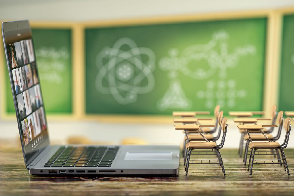 Giant laptop in front of tiny desks and a chalkboard