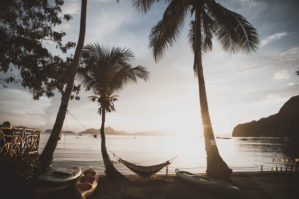Sunset beach with a hammock swaying between palm trees.