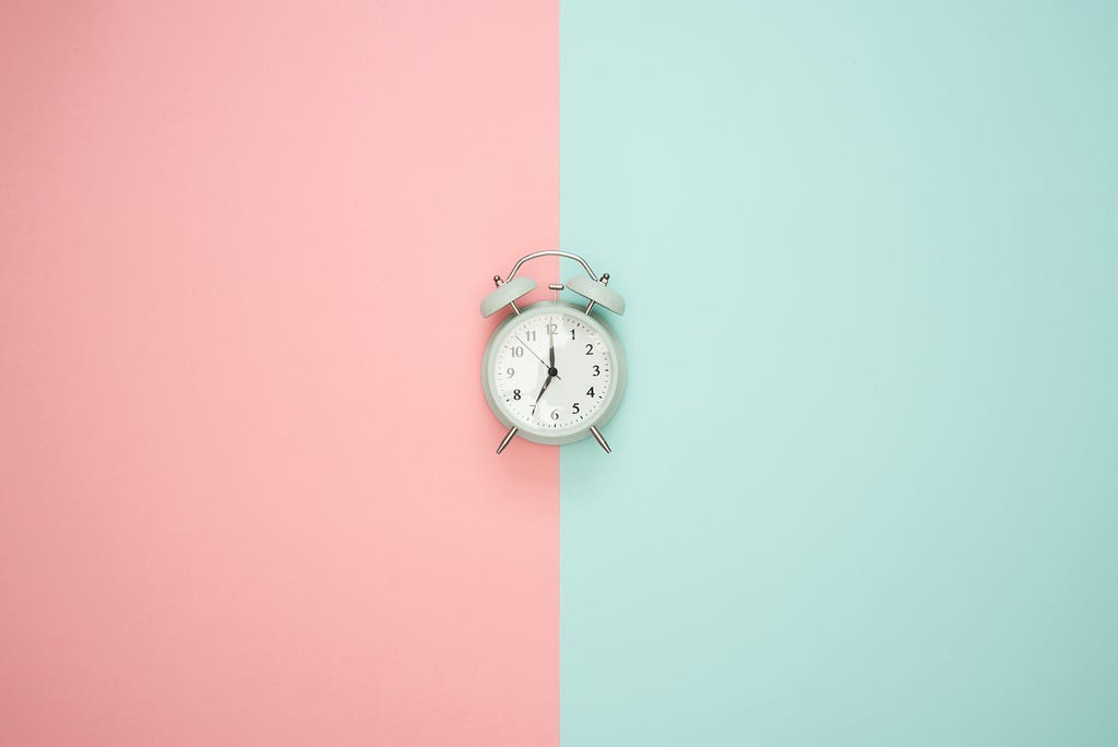 An alarm clock positioned at the center, with a background in soft pastel tones of pink and blue.