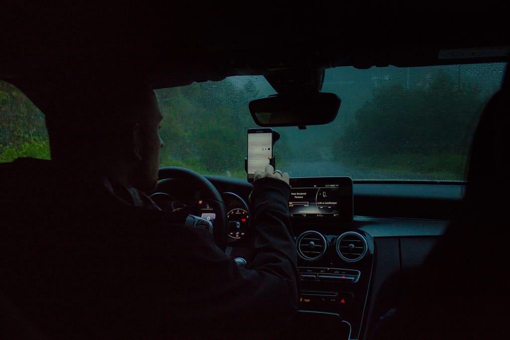 A man in the car, in dark, setting his GPS to a location, and following it.