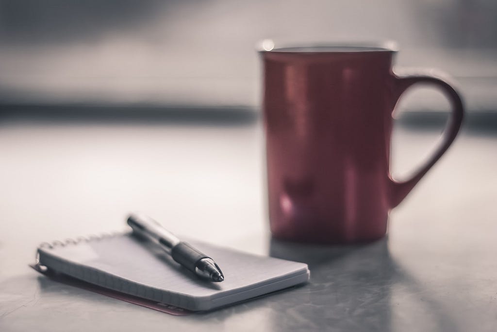 Photo of a notepad and pen next to a coffee mug