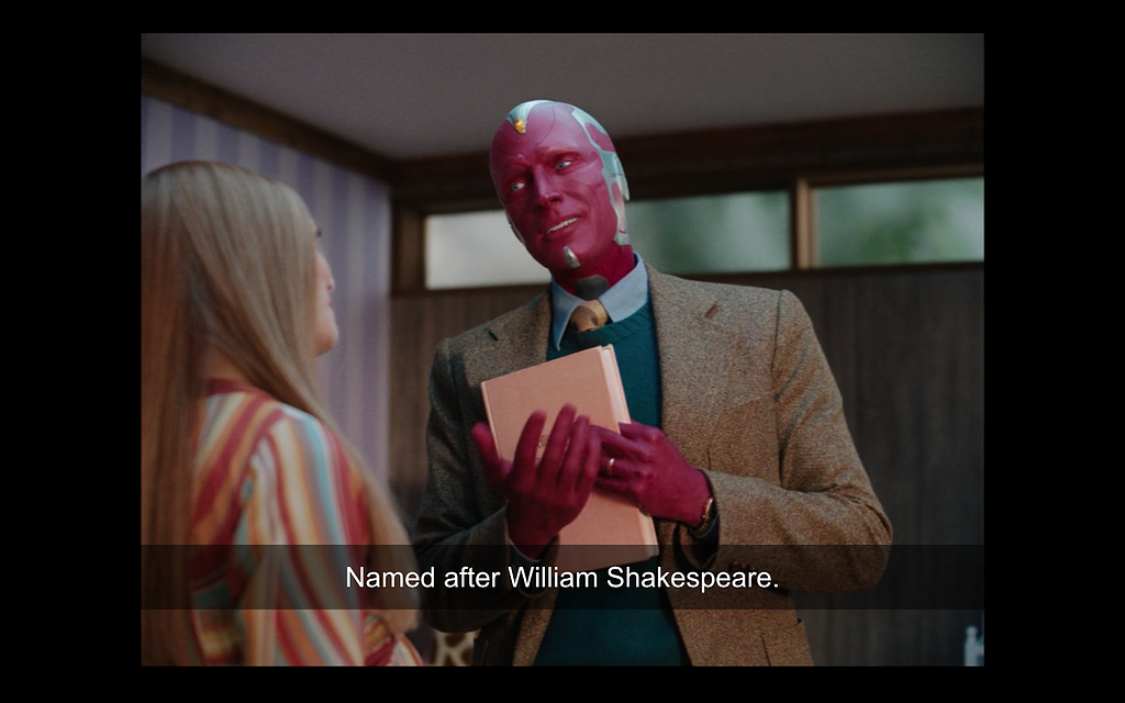 Vision (from the Dinsney+ show “WandaVision”) stands in front of Wanda clutching a book to his chest.