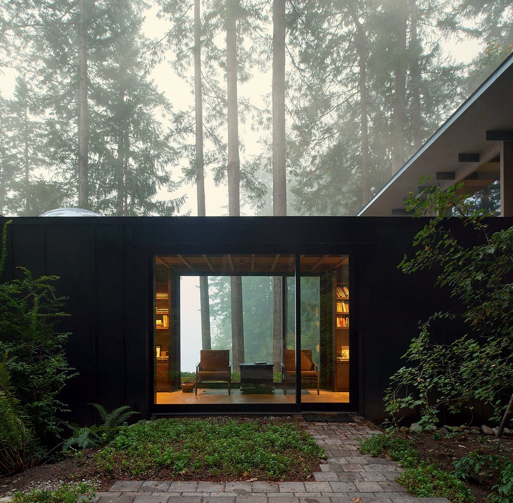 Outdoor, Back Yard, Woodland, Walkways, and Shrubs The cabin is intentionally subdued in color and texture, allowing it to recede into the woods and defer to the beauty of the landscape.&nbsp;