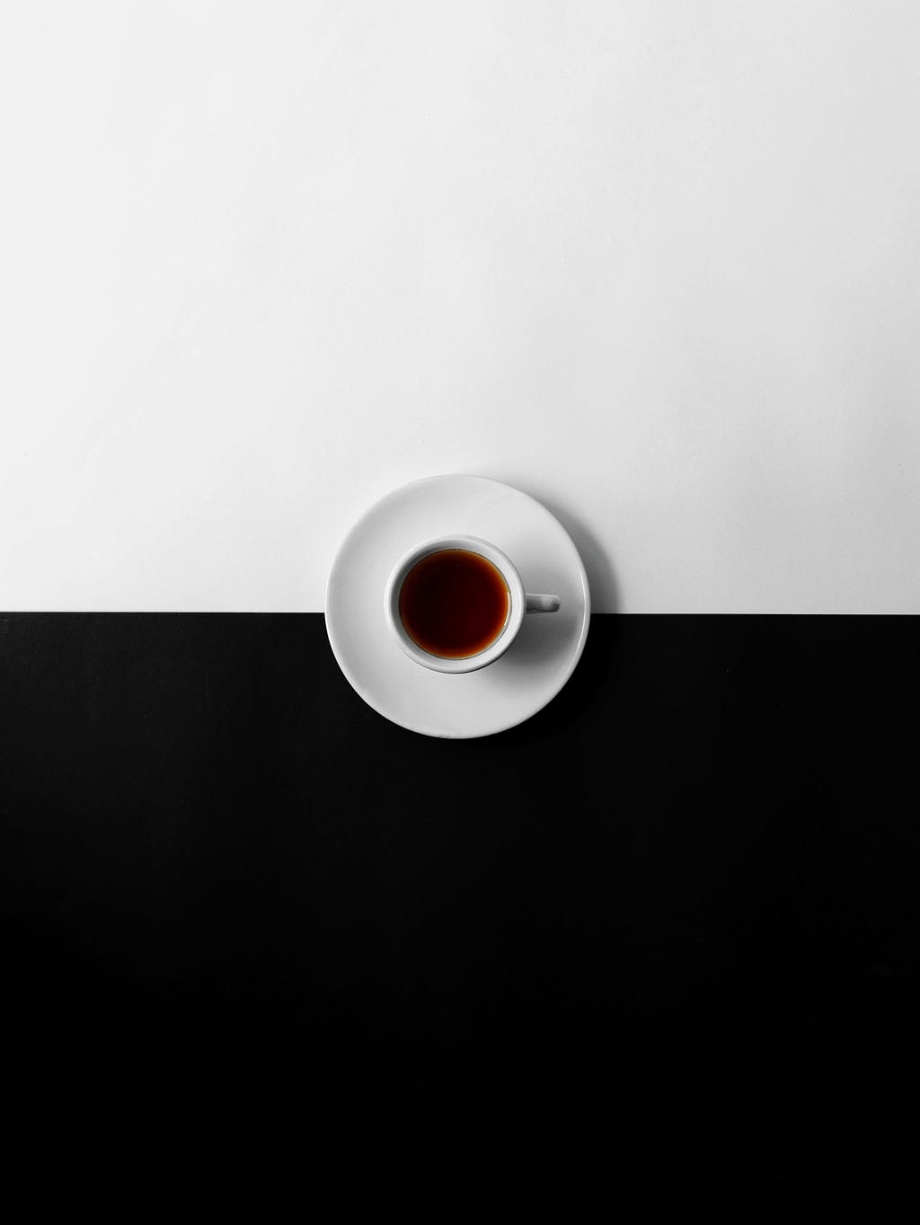 A white cup of black coffee isolated on a white and black background