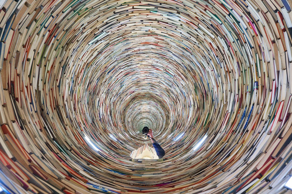Um túnel de inúmeros livros com um espelho à sua base, causando uma sensação de espaço infinito.