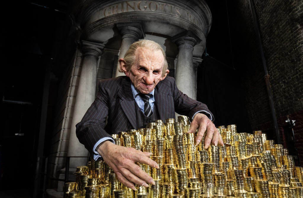 A promotional image for one of the Harry Potter movies, featuring a Gringotts Bank Goblin hugging a pile of gold coins, with the Gringotts bank facade behind him.