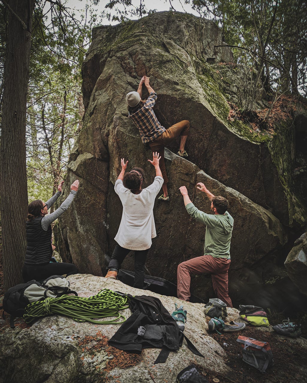 Three friends spotting a fourth, who is bouldering up the side of a rock.