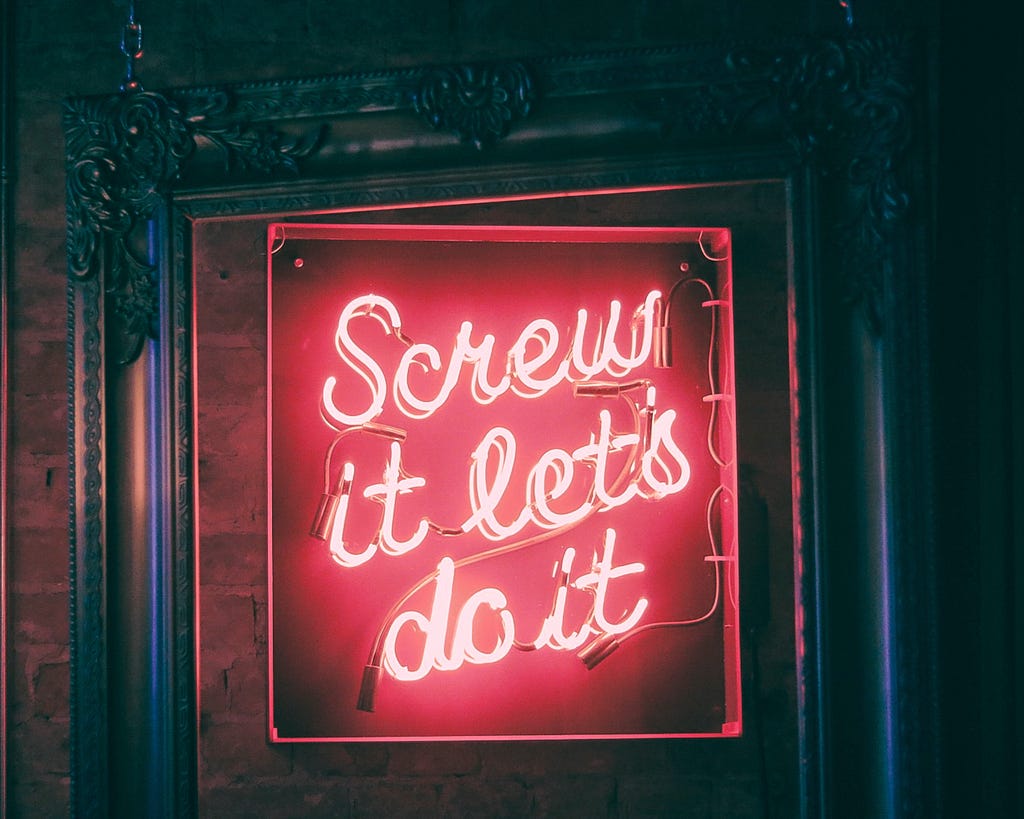 Neon sign with the words “Screw it, let’s do it” emblazoned in red.