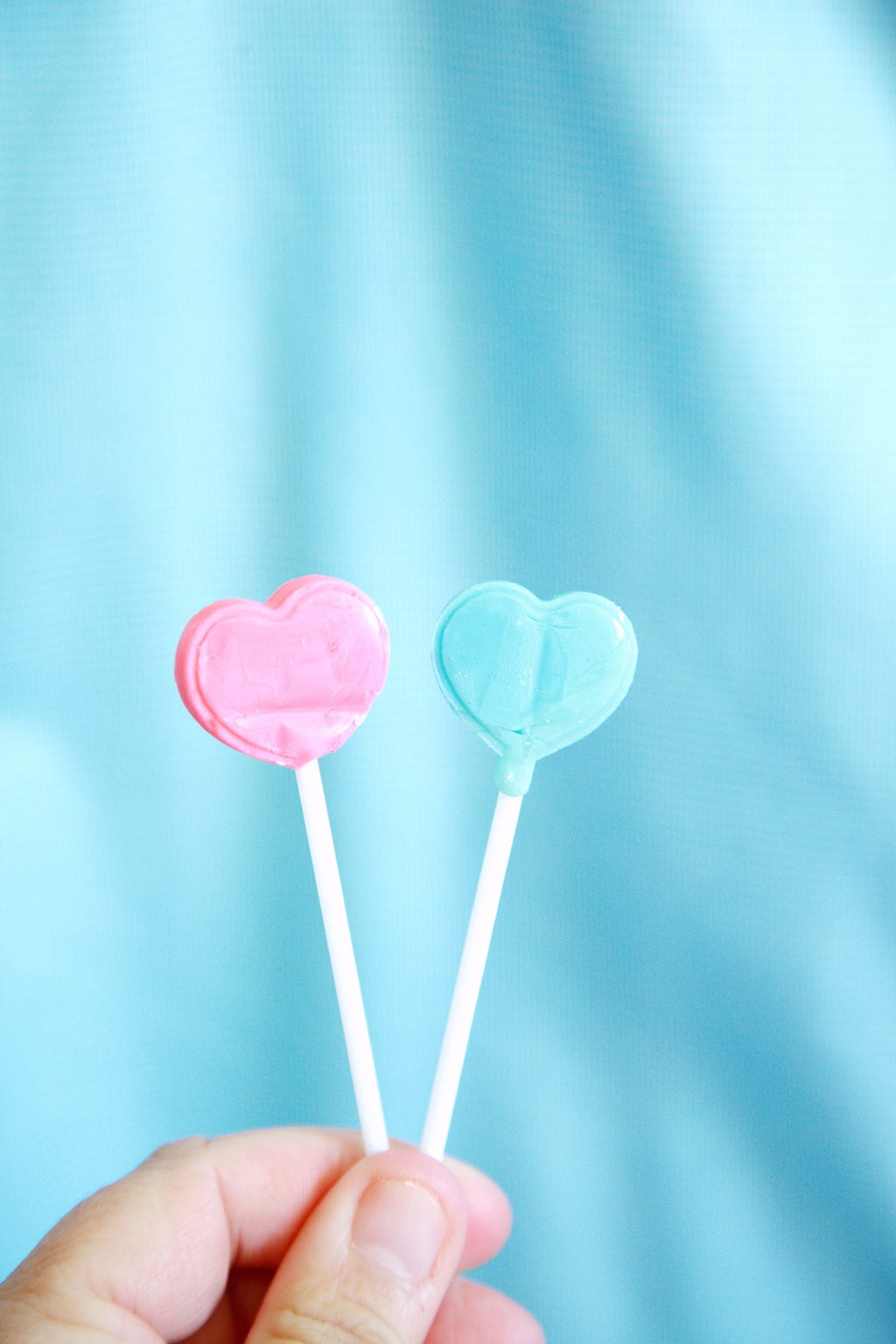 Two lollipops. One blue, one pink against a blue fabric background.