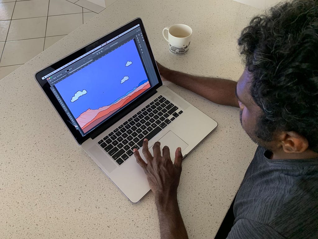 A photograph of a person on a laptop playing the game. On the screen there is a computer graphic of a desert landscape. Beside the person is a coffee cup on a table.