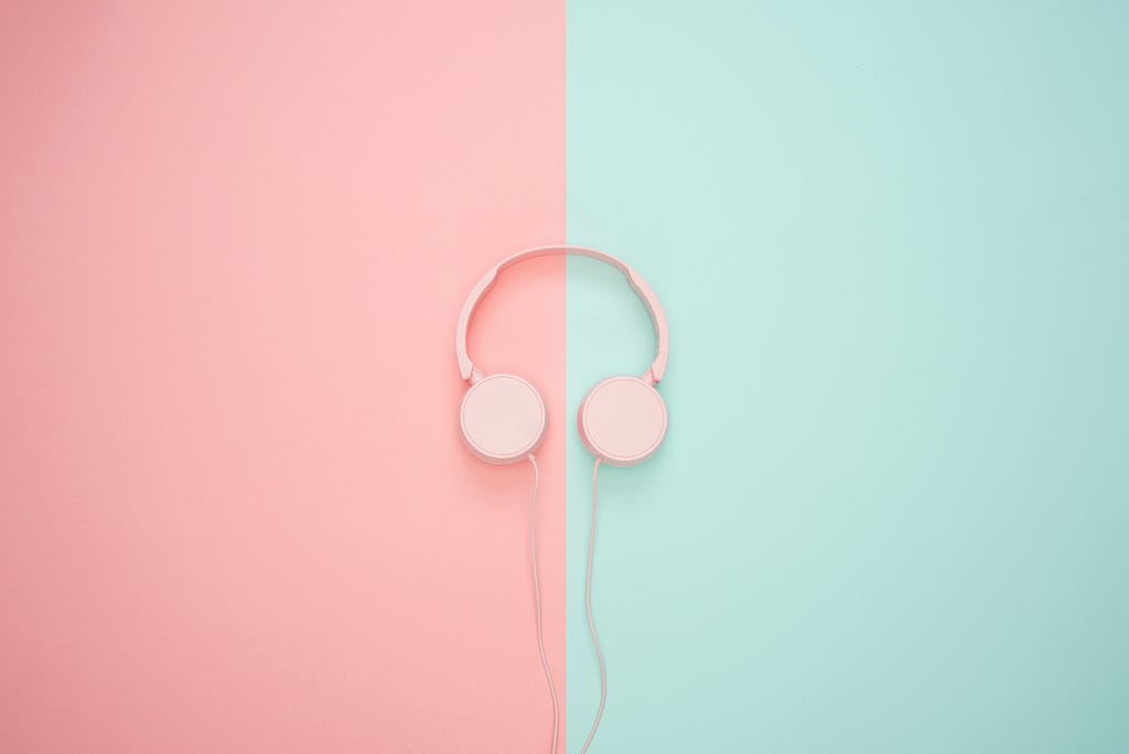 A pair pink of headphones with a pink wire is placed in the centre of the image. The background is split down the middle. The left side is pink, the right side is green.