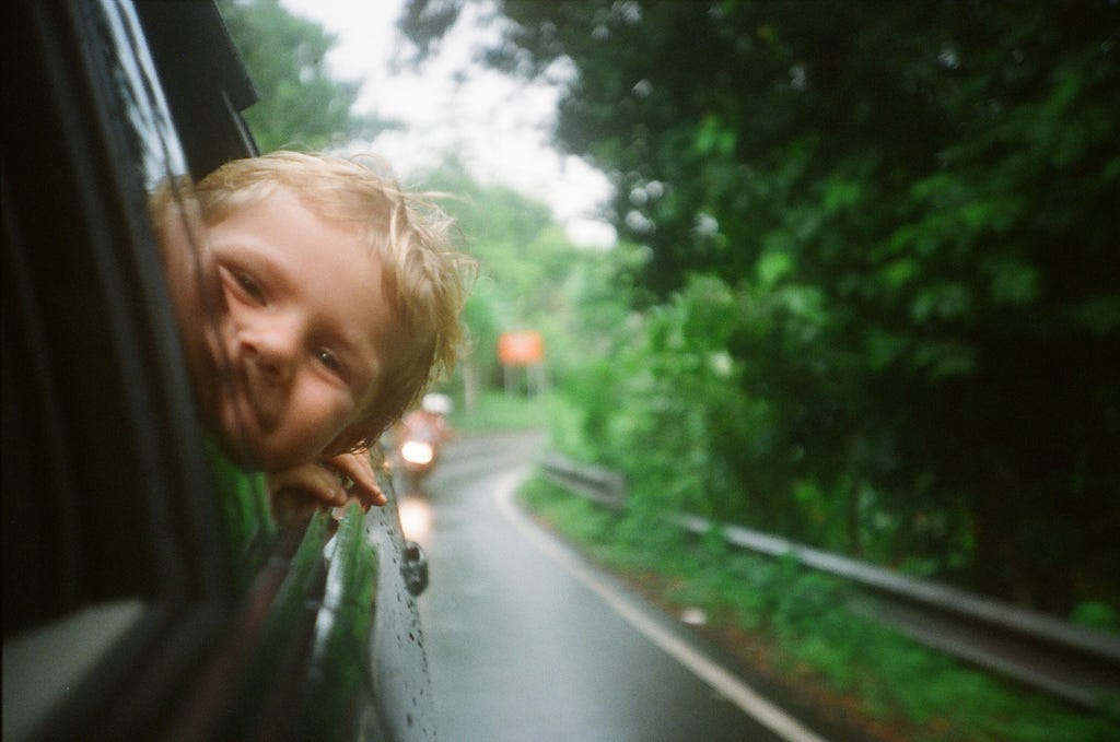 Young boy smiling and sticking his head out of a car window