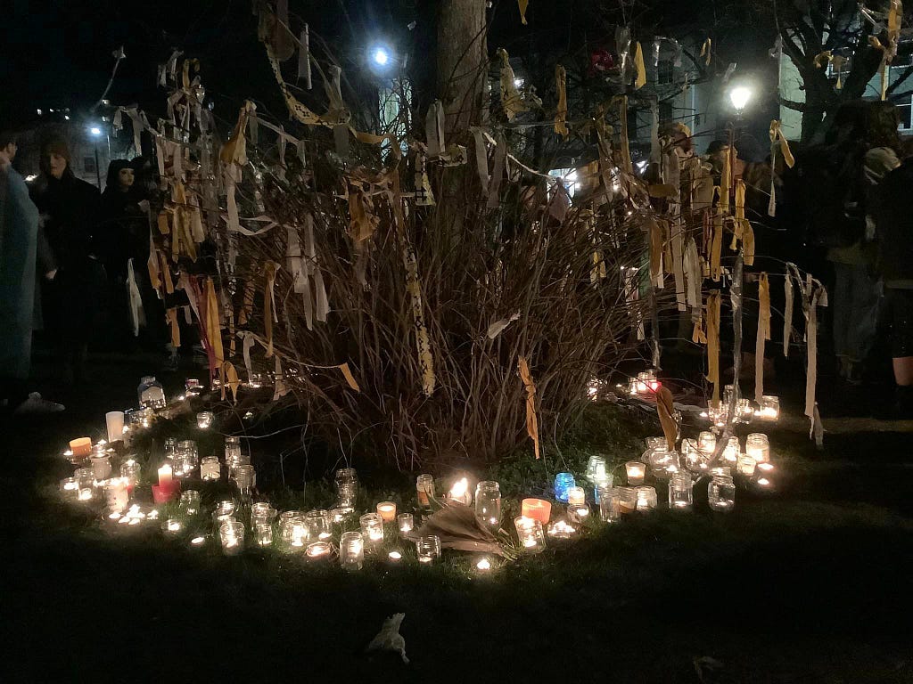 The Trans Memorial Tree in Bristol, wreathed in ribbons for our lost siblings, surrounded at the base with the candles of our vigil.