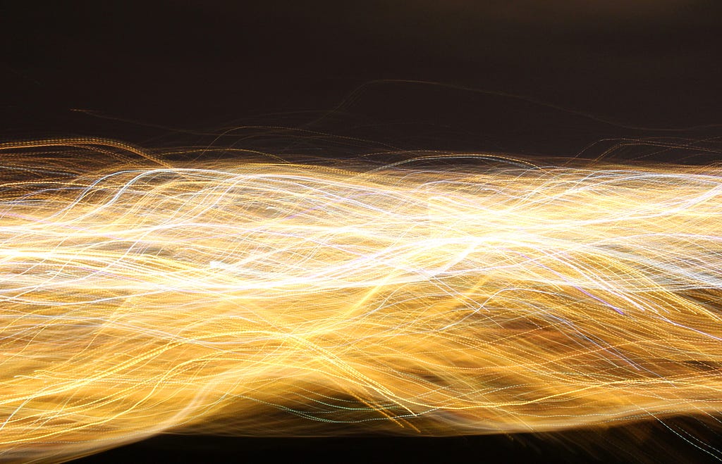 Thin fibers lit from within across a dark backgroound. Abstract image.