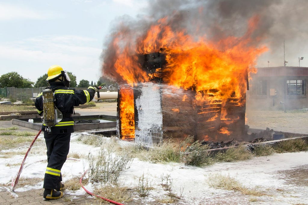 A firefighter sprays water from a hose on a small burning building.