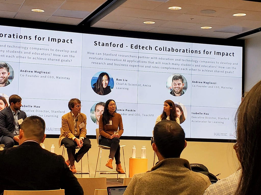 Four people sitting on stage facing the crowd with presentation slide behind them titled “Stanford-Edtech Collaborations for Impact”