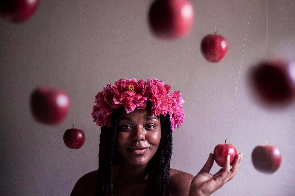A woman with a flower crown holding a red apple