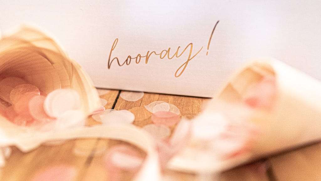 A white piece of paper with “Hooray” written in gold script.