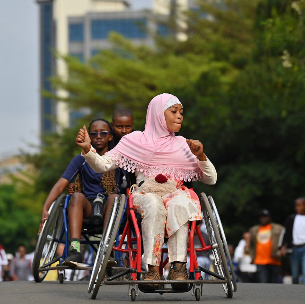 A Tanzanian woman in a wheelchair moves to music in a public street