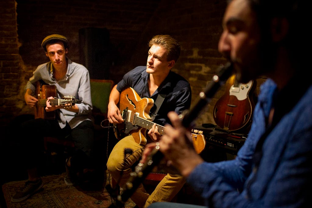 Two men playing guitar, one main playing an oboe.