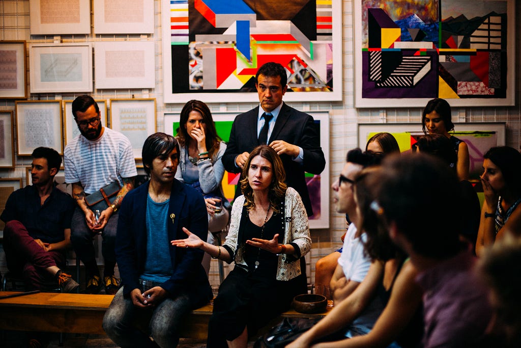 Uma reunião de onde uma mulher esta ao centro conversando e trocando ideais.