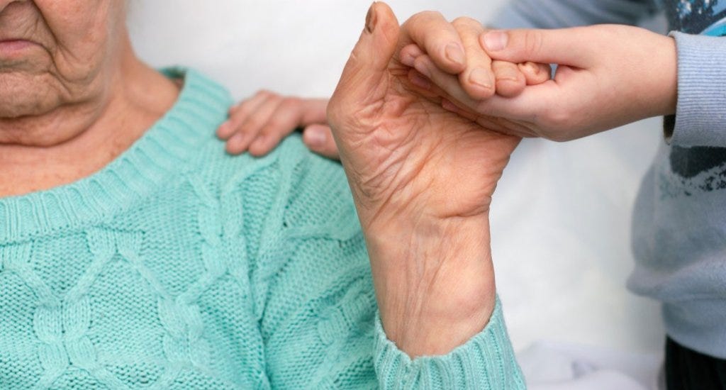 A caregiver holding the hand of an elderly woman