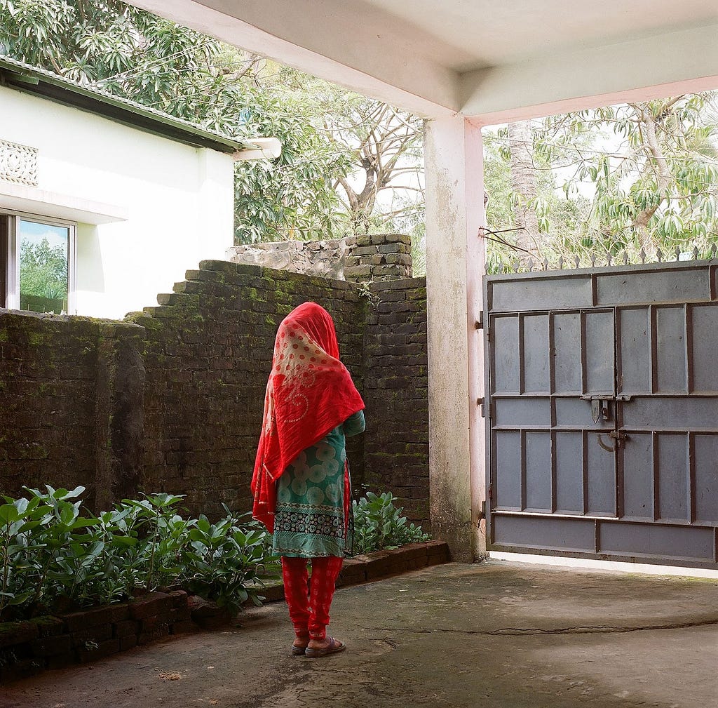 An image of a woman looking past her gates from where she lives