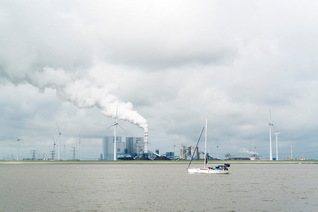 a boat on a river with wind mills and a smoking factory chimney in the background
