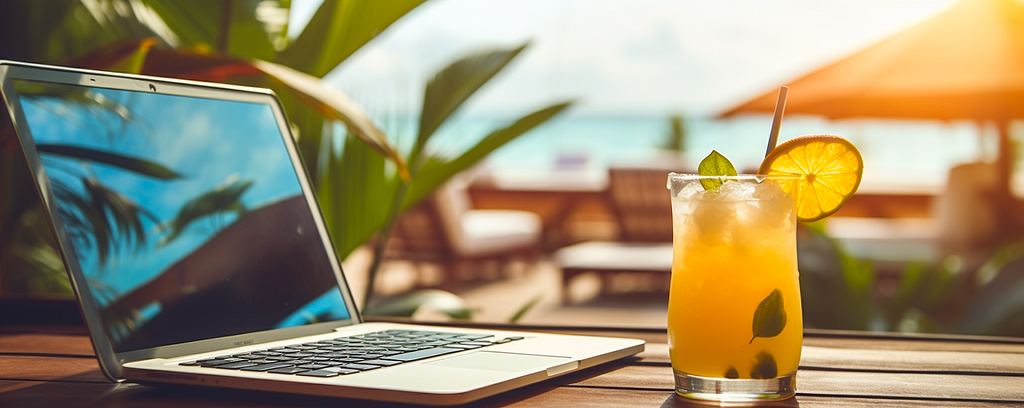 Turned off laptop and exotic tropical cocktail on wooden table at a resort terrace with beach chairs and ocean in background