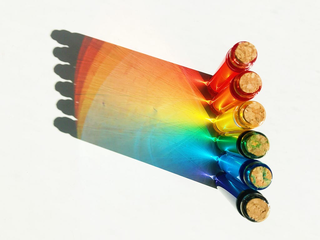 A ray of light going through small bottles in different colors, having as a reflection the colors of the rainbow.