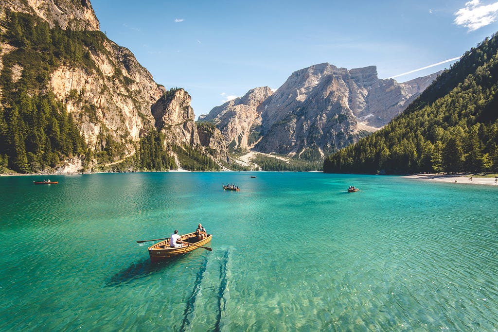 Travelers boating in a clear bluish-green lake overlooking beautiful mountains and trees