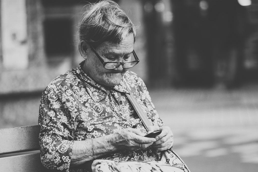 Elderly woman sitting on a bench, holding a mobile phone