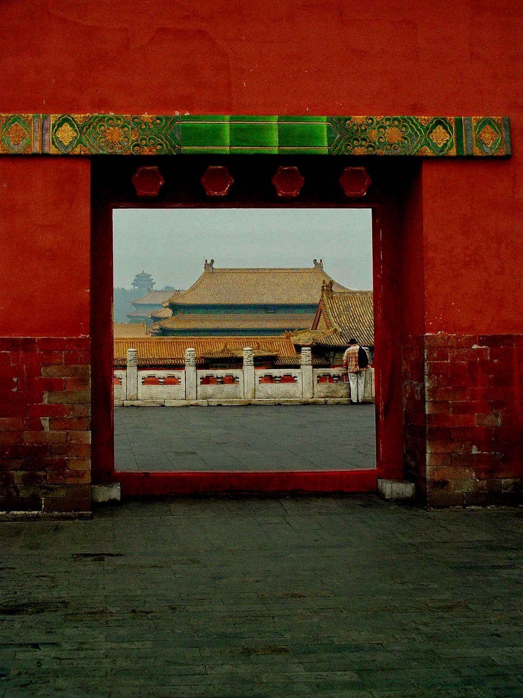 Red wall and a square opening looking through to rooftops at Forbidden City in Beijing, China.