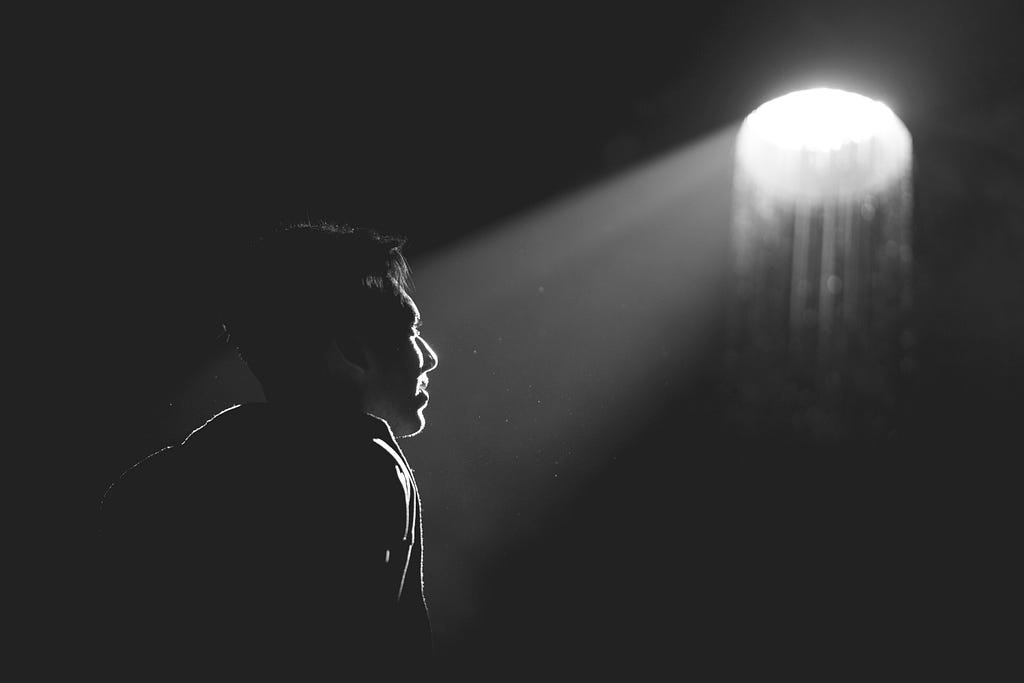 A man in a very dark room staring at a white orb of light.