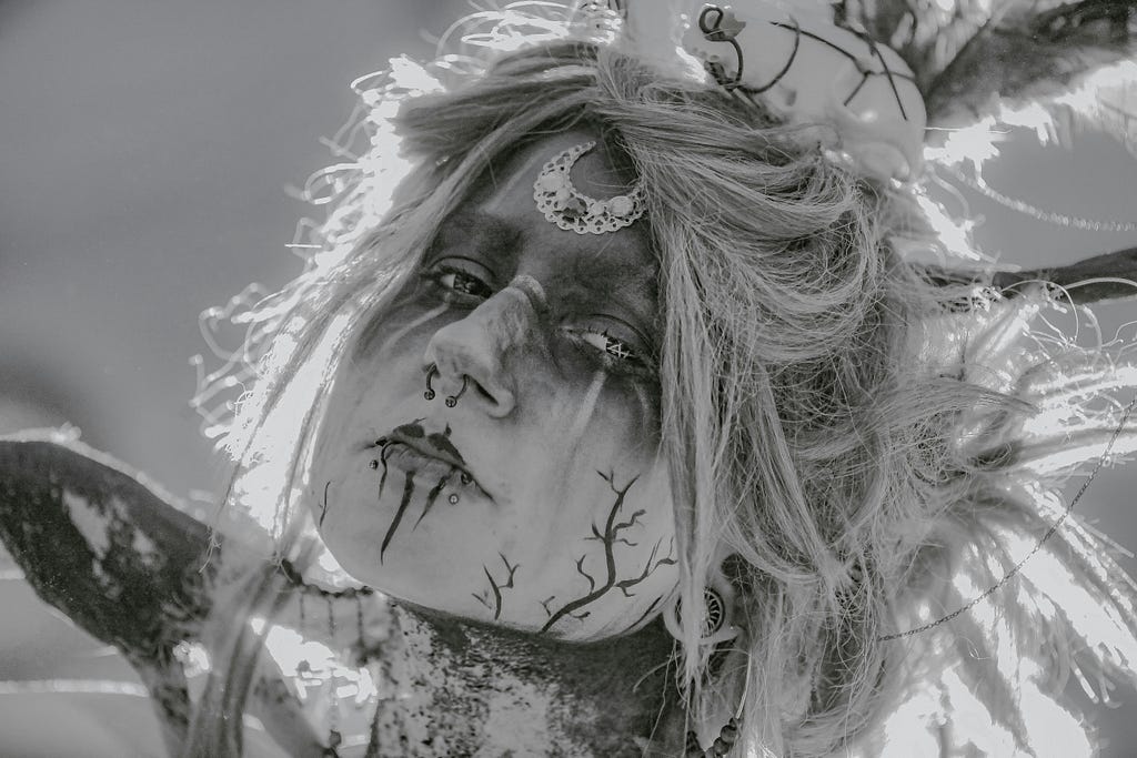 A photograph of a woman who is on a journey into the underground forest, the liminal world between worlds. Tangled hair, face paint and nose piercing.