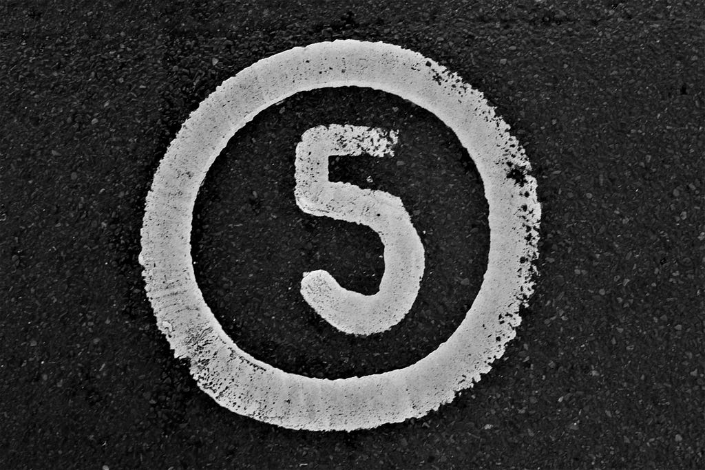 The numeral five handwritten in white, chalky looking paint on a dark gray concrete. The number is circle in the same white paint.