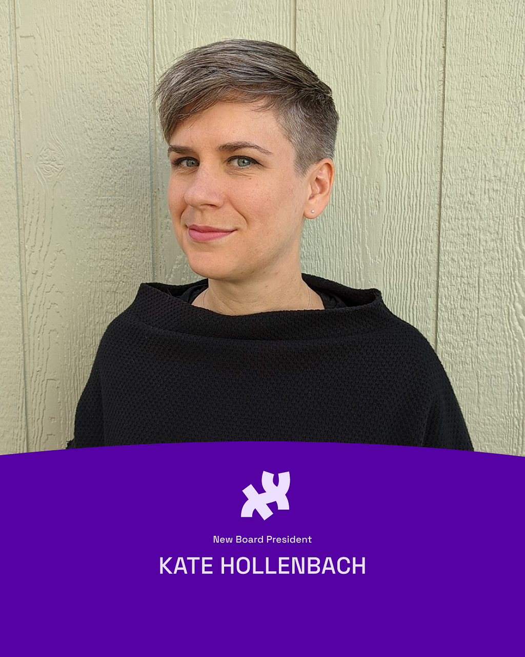 Kate is wearing a black sweater, standing in front of some light green paneling. She has pale skin and short, cropped gray hair. She looks at the camera with a shy smile. Their profile photo sits on top of a dark purple graphic element at the bottom in the shape of a hill, which reads, “New Board President Kate Hollenbach” with the Processing logo in white on top of the text.
