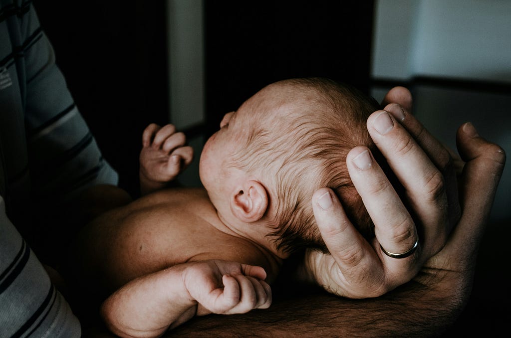 An Infant being held in a man’s hands.