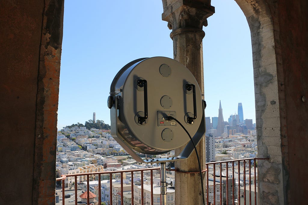 A large speaker (LRAD) facing the cityscape of San Francisco, the installation is housed at the top of a tower overlooking the city